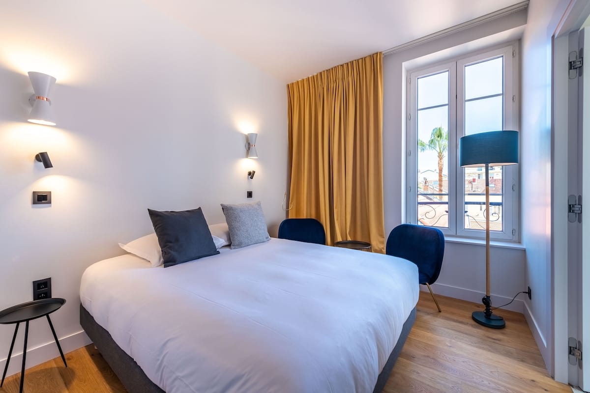 A hotel room with a large bed, two wall-mounted lamps, a desk, and a chair.
