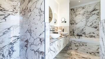 A bathroom with marble flooring and walls, a glass-enclosed vanity, and a modern shower area.