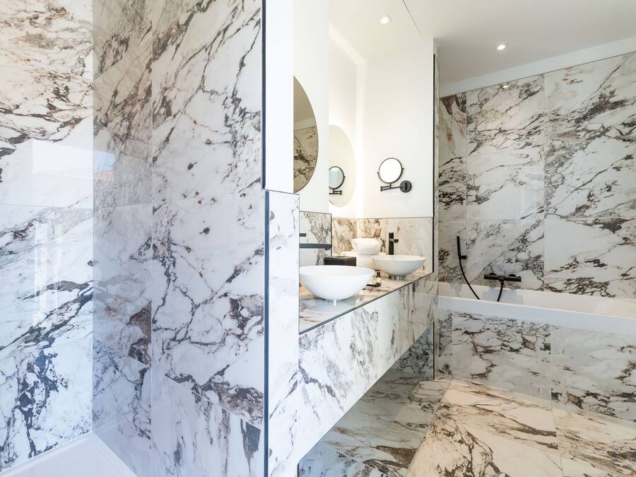 Une salle de bain avec un sol et des murs en marbre, un meuble-lavabo entouré de parois en verre et une douche moderne.