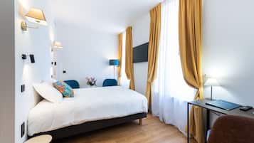Una habitación de hotel moderna con una cama, un escritorio con lámpara, una silla y una pequeña mesa.