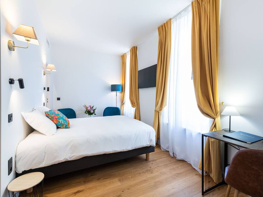 Una habitación de hotel moderna con una cama, un escritorio con lámpara, una silla y una pequeña mesa.