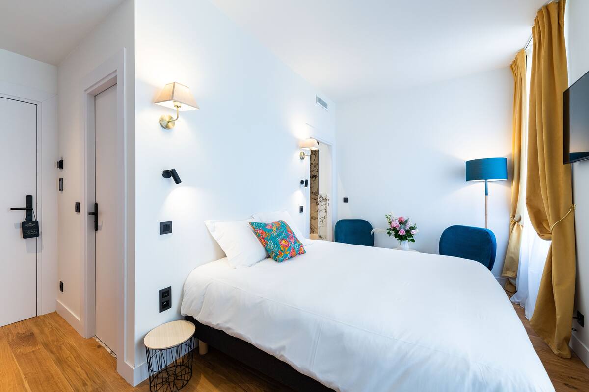 A modern hotel room with a large bed, bedside lamps, a flat-screen TV, a small round table, and a chair.