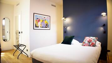A bedroom with a bed, a mirror, a painting, and wall-mounted lights.