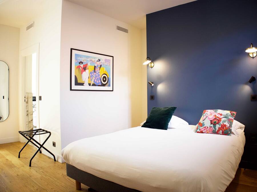A bedroom with a bed, a mirror, a painting, and wall-mounted lights.
