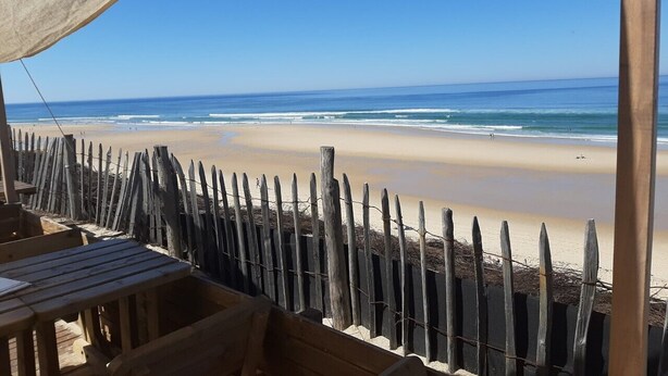 A beach view with a wooden fence and a table under a shaded area. - Vacation home with heated pool (La Teste-de-Buch)