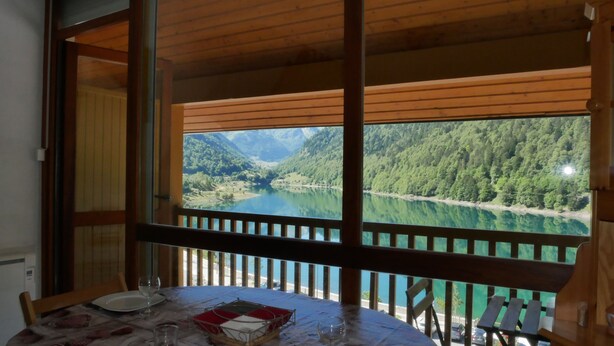 A dining area with a table set for two, overlooking a lake and forested mountains. - 5-bed apartment with superb view of Lake Artouste (Laruns)
