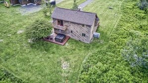 A two-story wooden house with a balcony, surrounded by a grassy yard and a road in the background. - YR10- AC! Pet Friendly! Hot tub! (Davis)