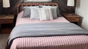 A bedroom with a wooden slat wall, a window, a bed with pink bedding, two bedside tables with lamps, and a wooden headboard. - YR10- AC! Pet Friendly! Hot tub! (Davis)