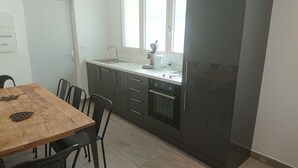 A compact kitchen with a wooden dining table, black chairs, a built-in oven, and a window above the sink.