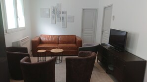 A living room with a brown leather sofa, two round coffee tables, and a television on a wooden cabinet.