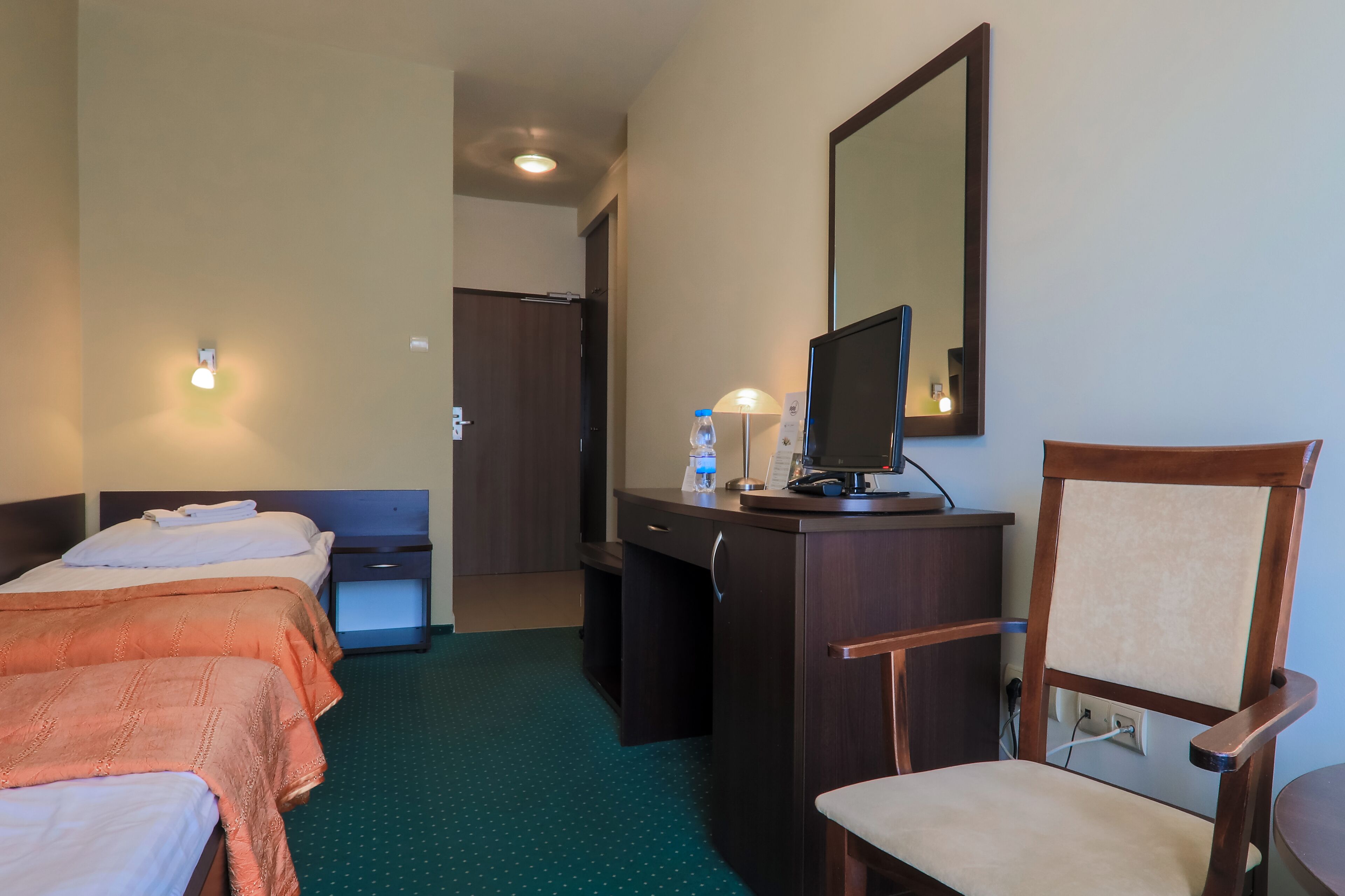 A hotel room with two beds, a desk with a computer, a chair, and a mirror.