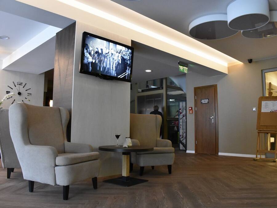 A lobby with two armchairs, a small table with a glass, a mounted TV, and a wooden easel with papers.