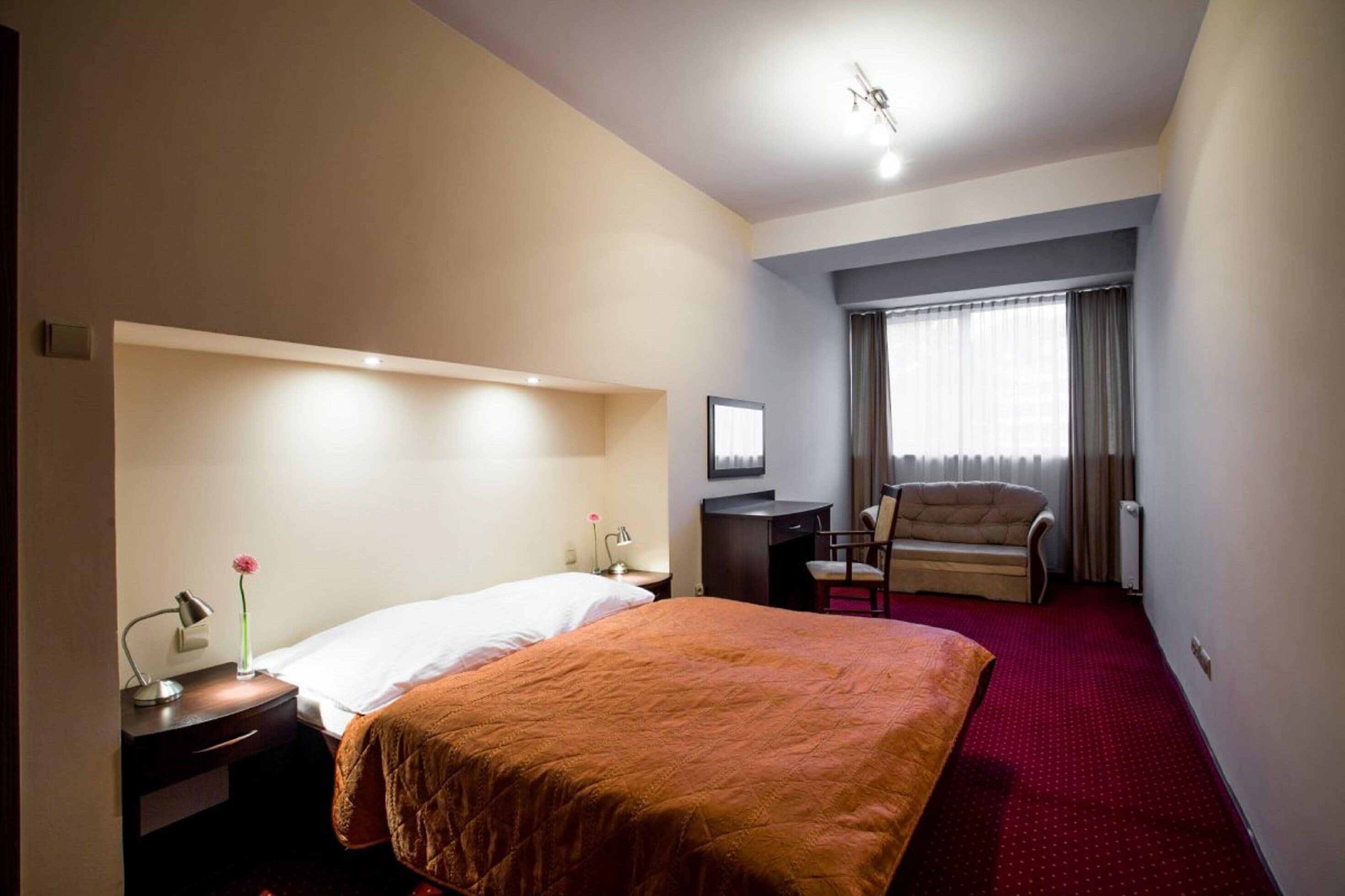 Una habitación de hotel con cama, escritorio, silla y ventana con cortinas.