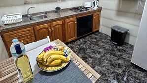 A compact kitchen with wooden cabinets, a microwave, a sink, and a table with a bowl of fruit and a bottle. - Holiday Home Casa del Molino with Sea & Mountain Views, Wi-Fi, and Terrace (Icod de los Vinos)