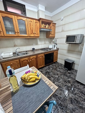 A compact kitchen with wooden cabinets, a microwave, a sink, and a table with a bowl of fruit and a bottle. - Holiday Home Casa del Molino with Sea & Mountain Views, Wi-Fi, and Terrace (Icod de los Vinos)