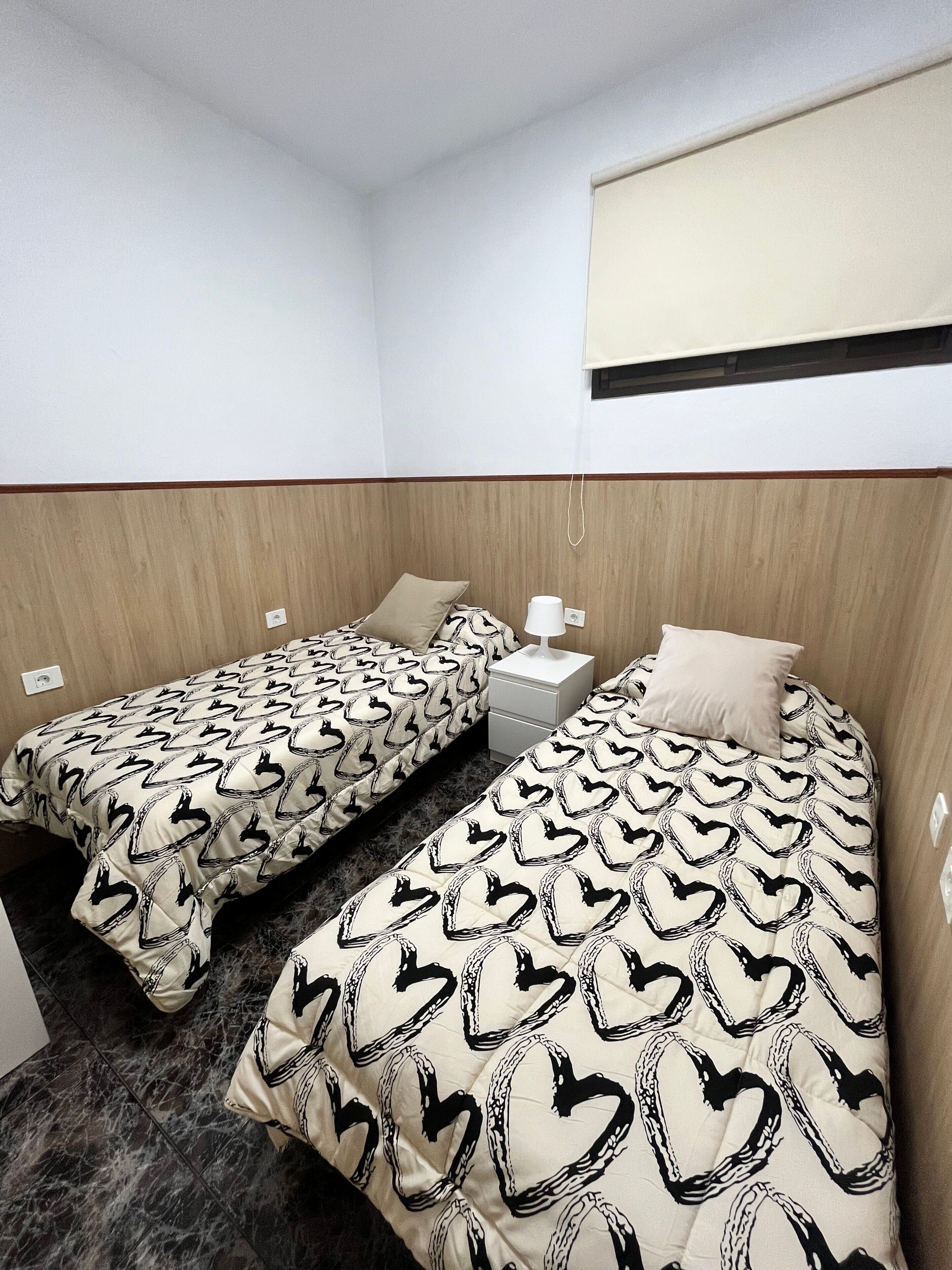 Quarto com duas camas, cada uma com colcha estampada, mesa de cabeceira com abajur e cabeceira de madeira.