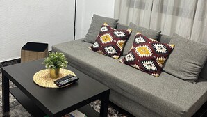 A living room with a grey sofa, two patterned cushions, a small table with a plant and remote control, and framed artwork on the walls. - Holiday Home Casa del Molino with Sea & Mountain Views, Wi-Fi, and Terrace (Icod de los Vinos)