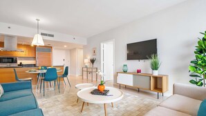Una sala moderna con un sofá, una mesa de centro con un libro, un televisor y un comedor con sillas y una mesa.