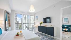 Habitación de hotel moderna con una cama grande, un escritorio, televisión y un balcón con vistas a la ciudad.