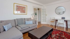 Un soggiorno moderno con un divano grigio, un tavolino, un tavolo da pranzo con sedie, uno specchio e un certificato incorniciato appeso al muro.