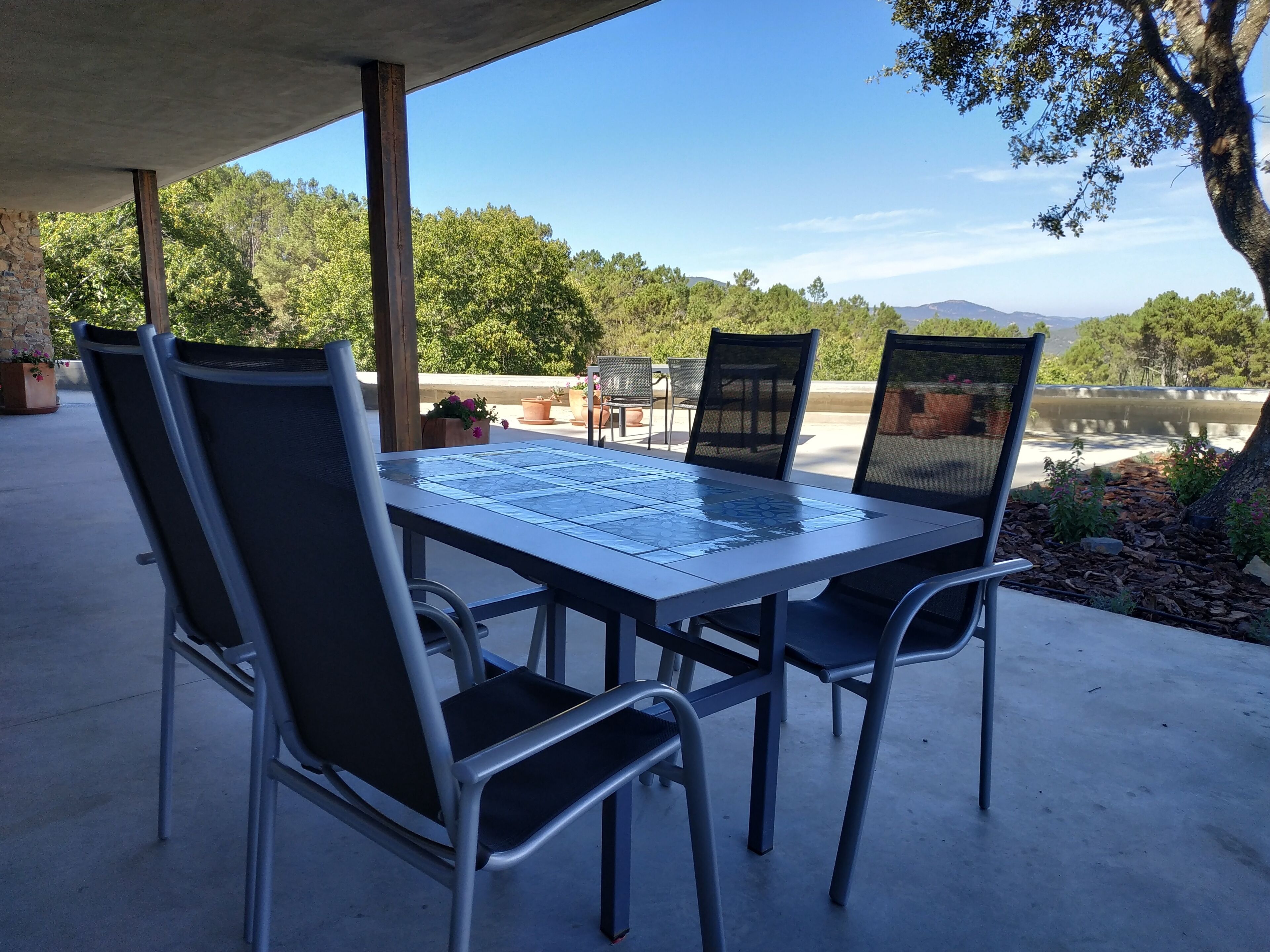 A covered patio with a table and chairs, overlooking a body of water and greenery.