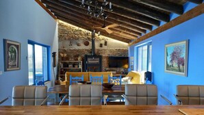 A rustic interior with a stone wall, wooden beams, a fireplace, and a dining area with a wooden table and chairs. - Madre del Agjua Rural House. Finca El Robledillo. (MONESTERIO)