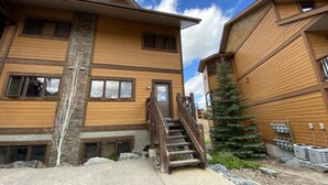 Un immeuble à plusieurs étages doté d’une façade en bois, d’un escalier menant à l’entrée et d’un petit arbre situé à proximité.