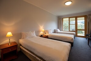 Een hotelkamer met twee bedden, een nachtkastje met een lamp, een stoel en een groot raam met uitzicht op het omliggende landschap.