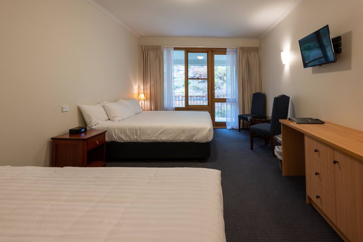 Ein Hotelzimmer mit zwei Betten, einem Schreibtisch mit Computer, einem Fernseher und Blick ins Freie.