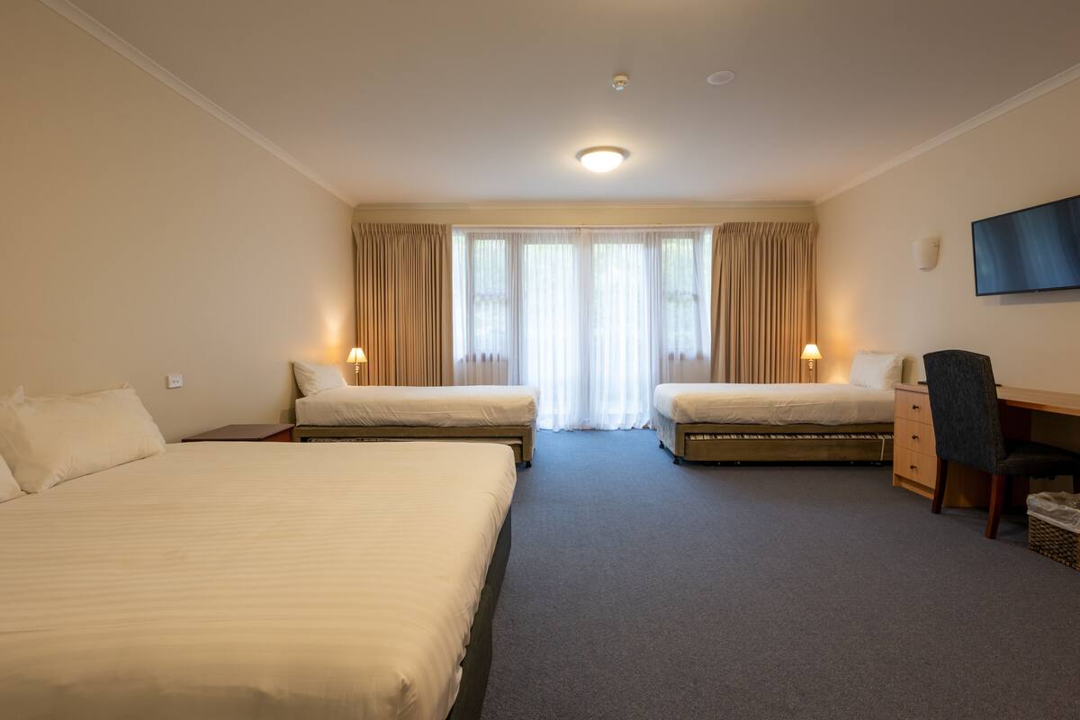 Ein Hotelzimmer mit zwei Betten, einem Schreibtisch, einem Stuhl und einem an der Wand befestigten Fernseher.
