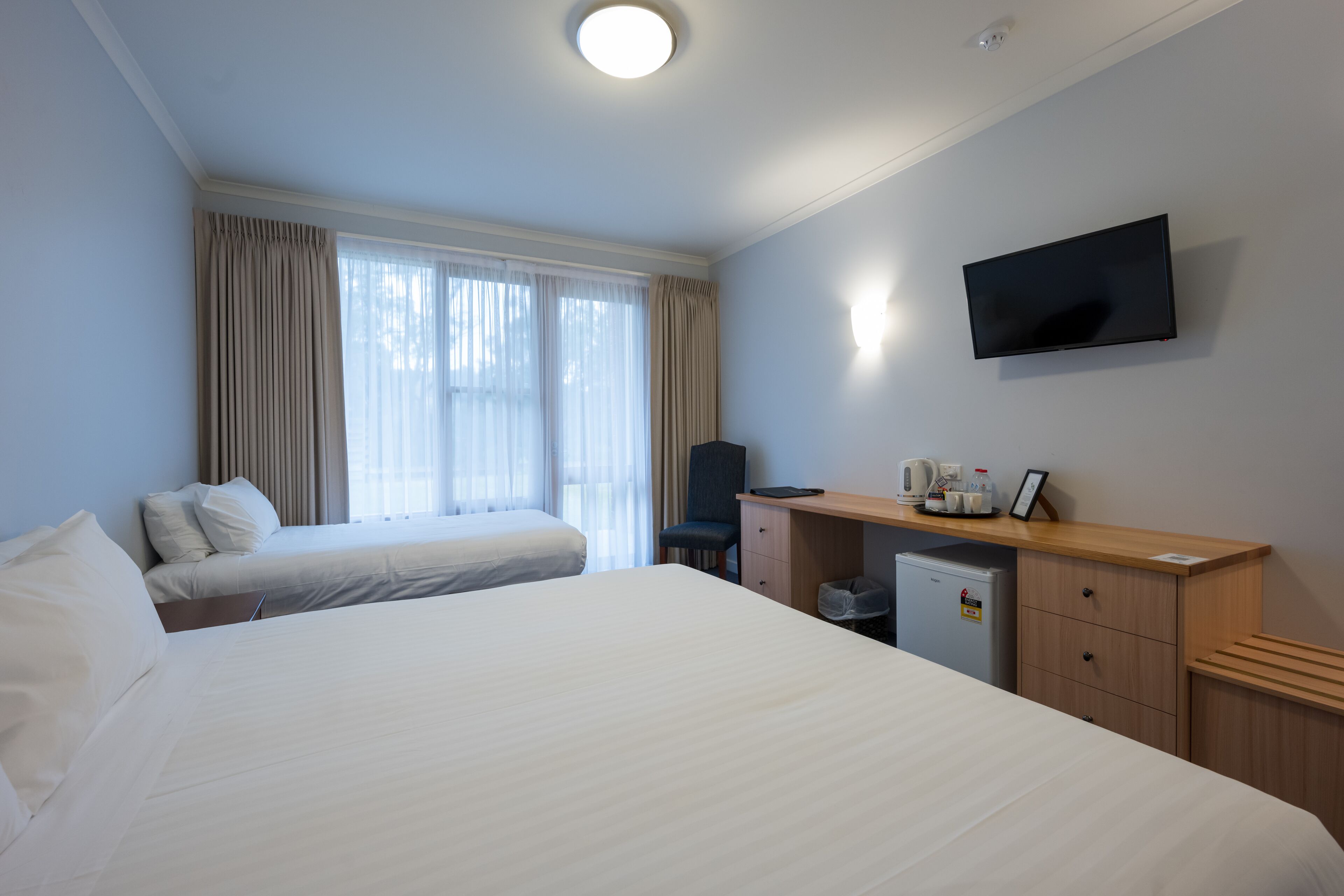 Una habitación de hotel con dos camas, un escritorio con televisor y una ventana con cortinas.