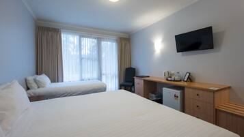 Una habitación de hotel con dos camas, un escritorio con televisor y una ventana con cortinas.