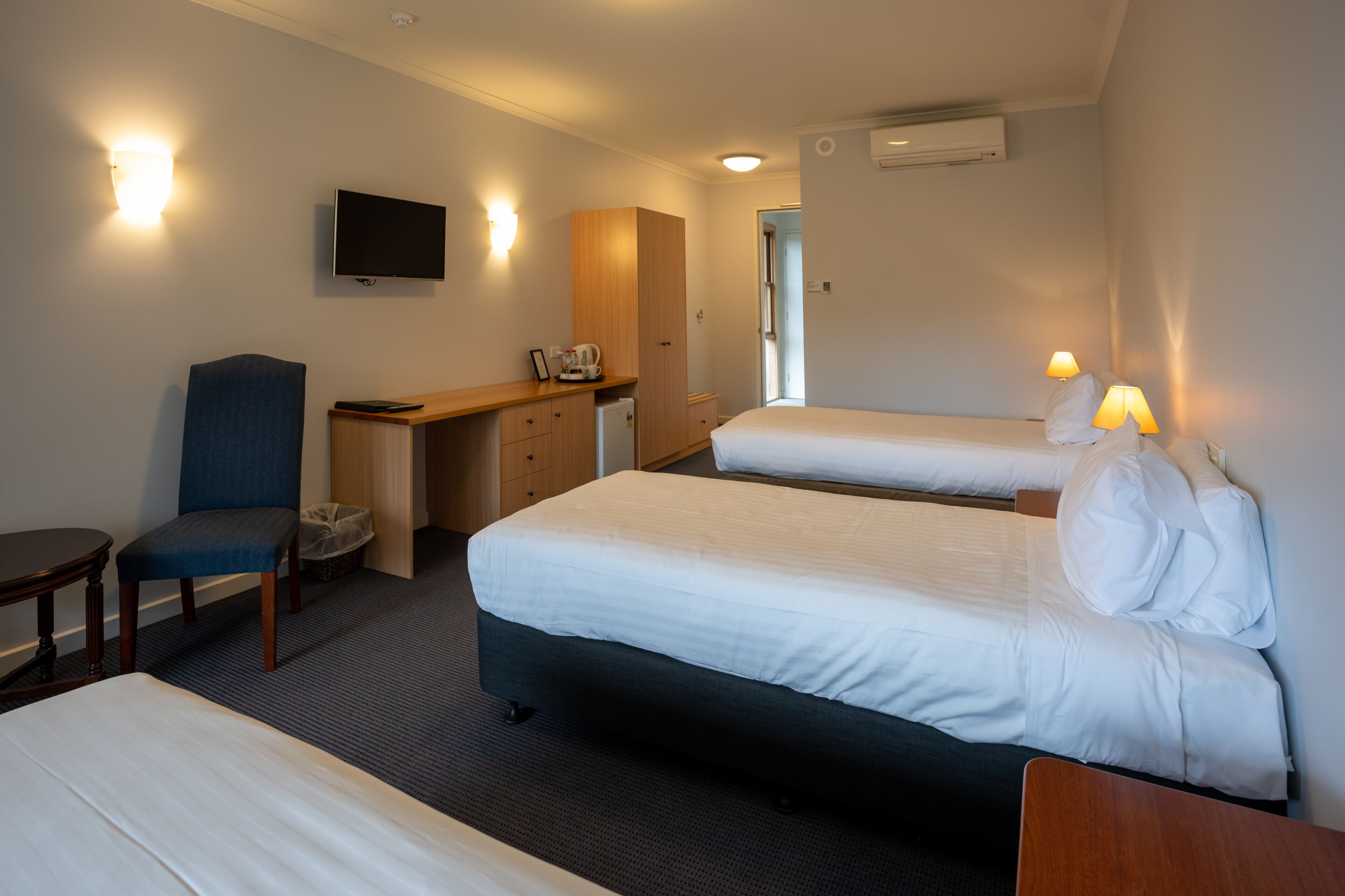 A hotel room with two beds, a desk, a chair, a TV, and a small table.