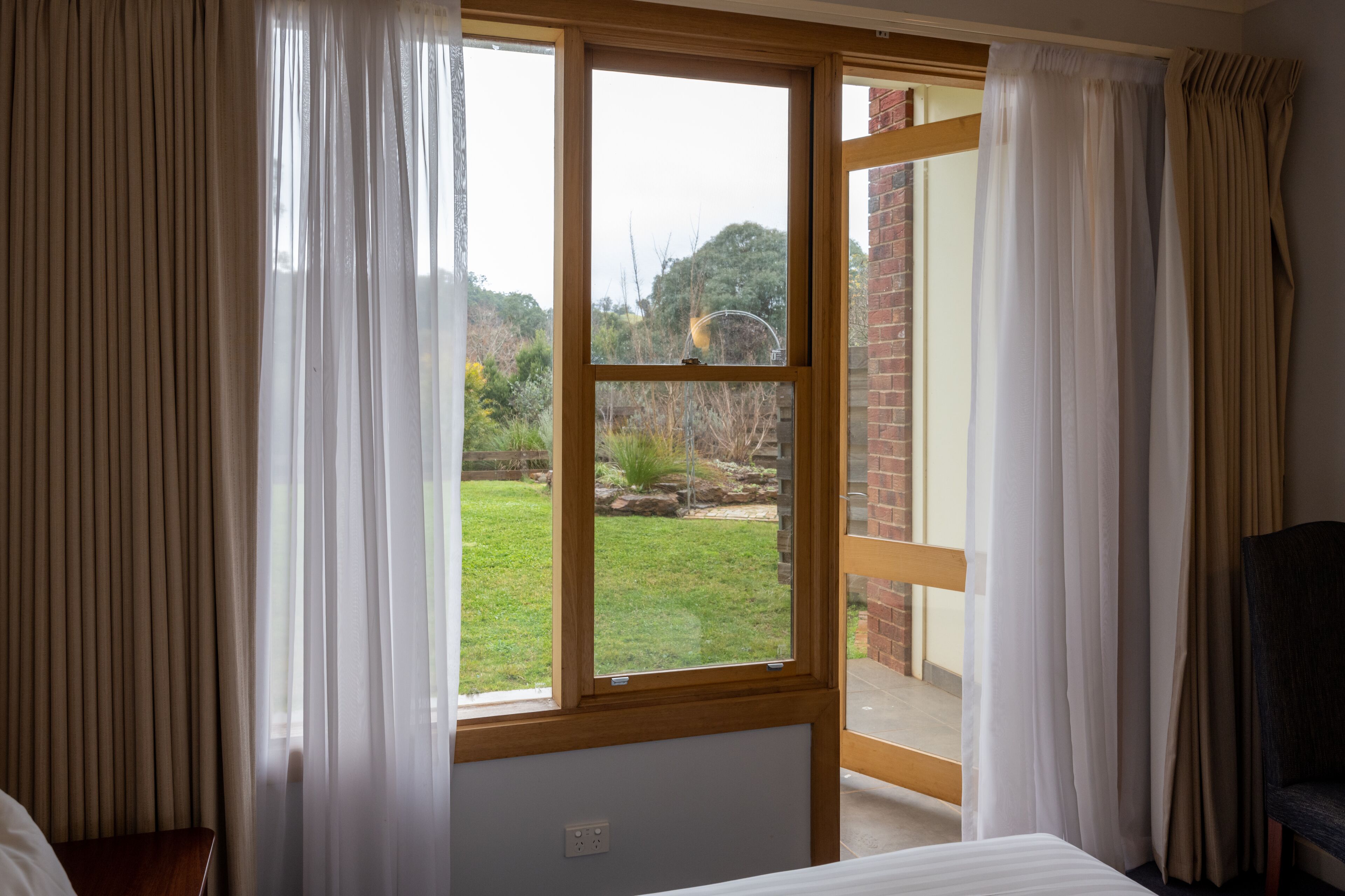 A bedroom with a large window, curtains, a bed, and a chair.