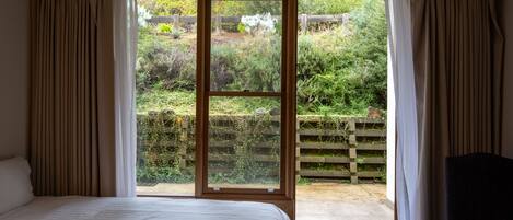 A bedroom with a large window, a bed, and a view of a garden.