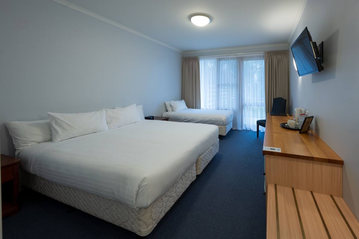 Ein Hotelzimmer mit zwei Betten, einem Schreibtisch, einem Flachbildfernseher und einem Fenster mit Vorhängen.