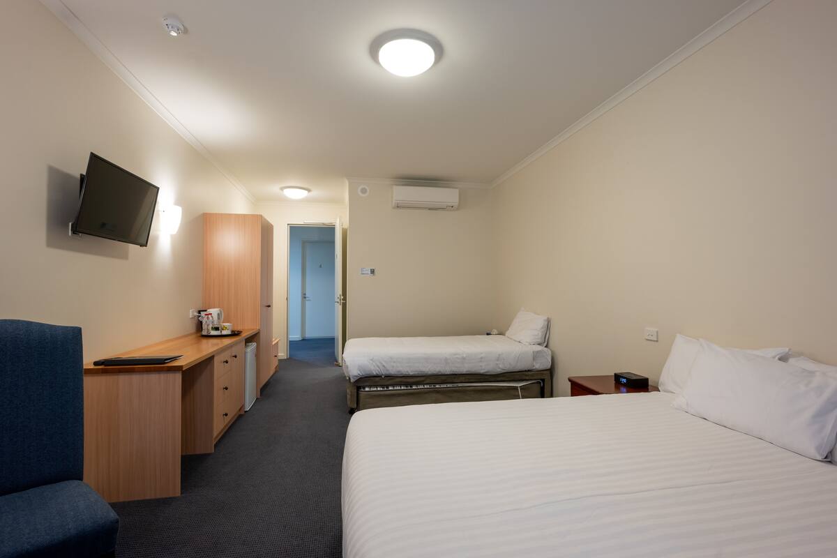 Ein Hotelzimmer mit Schreibtisch, zwei Betten, einem Fernseher und einer Tür zu einem weiteren Raum.