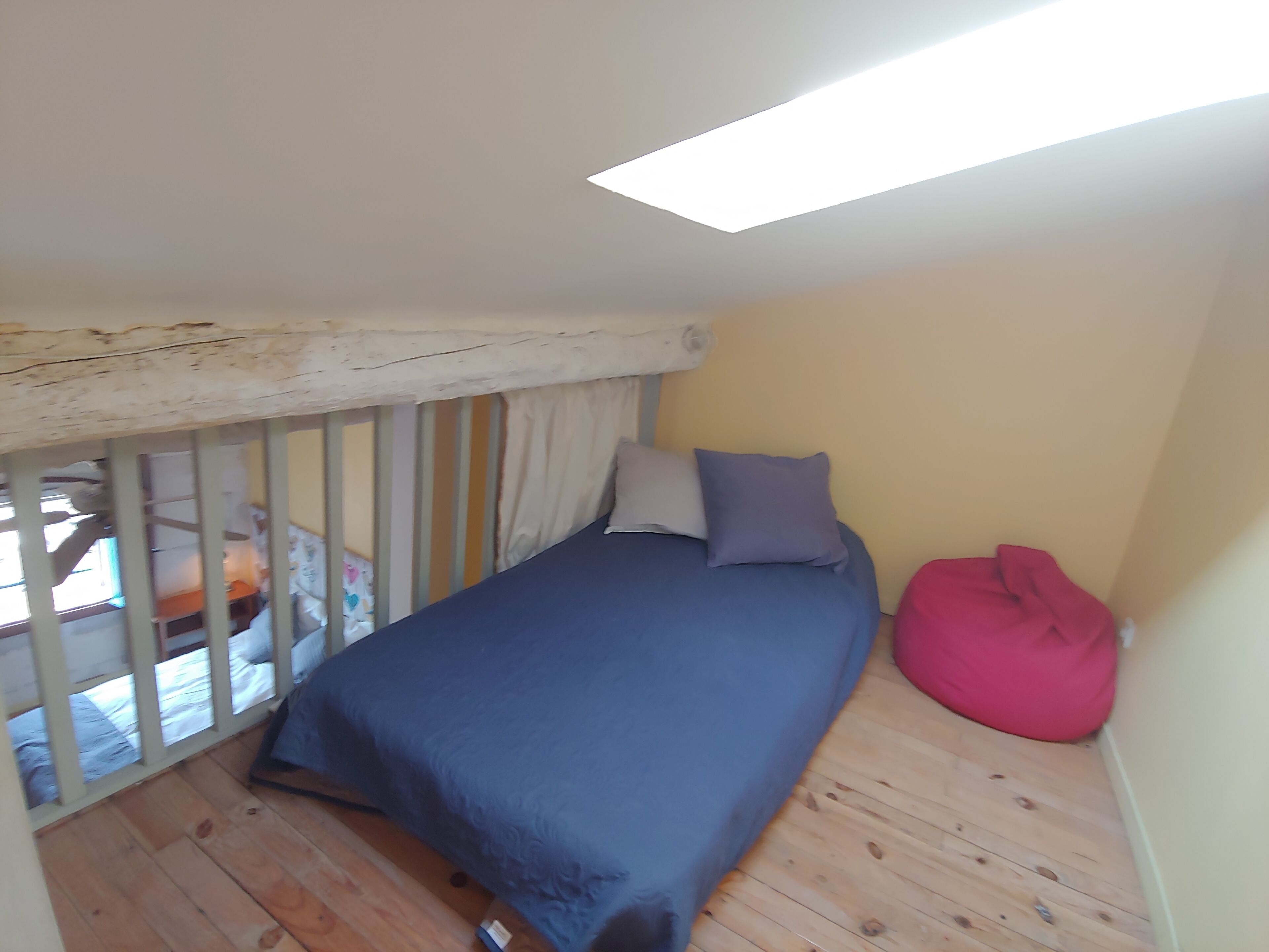 Una habitación pequeña con una cama individual, suelo de madera, techo inclinado y tragaluz.