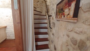 A staircase with white railings, a white wall with a thermometer, and a framed picture of fruits.