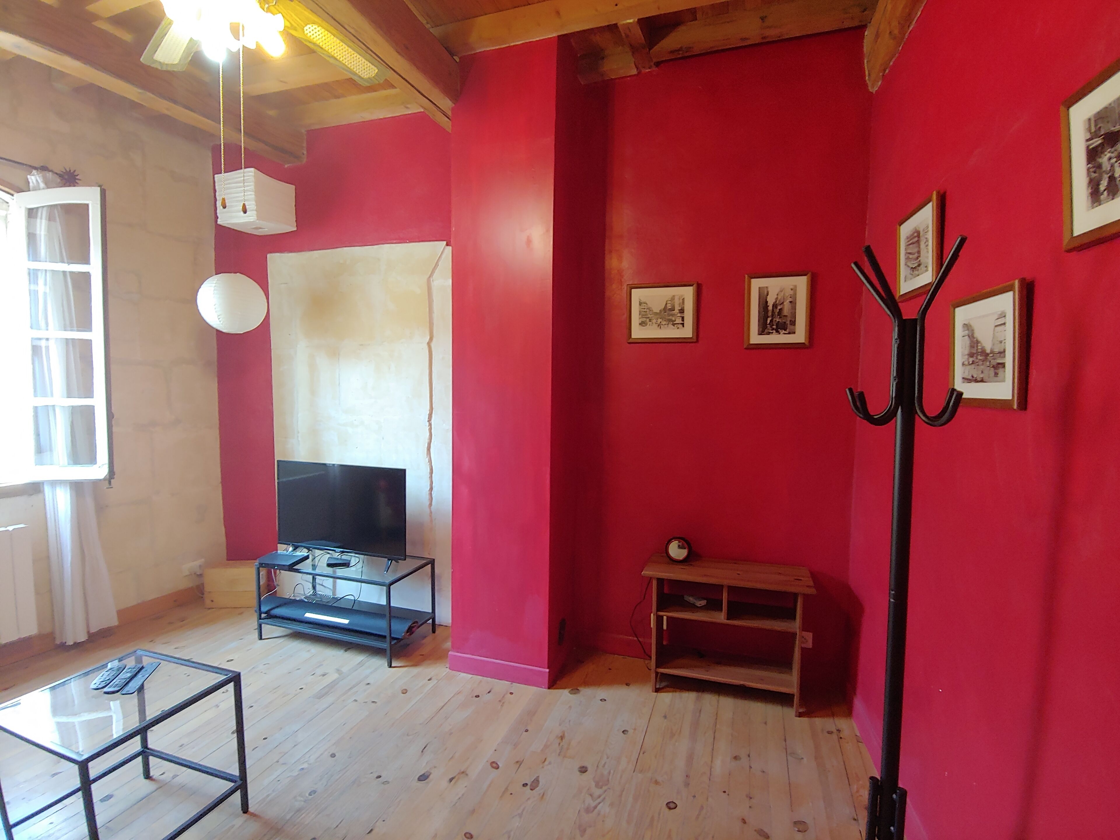 Een woonkamer met een rode wand, houten vloer, een tv-meubel, een glazen salontafel en een kapstok.