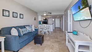 A living room with a blue sofa, a coffee table, and a flat-screen TV mounted on the wall. - Beachfront 2 Bed at Popular Seawinds! (Marco Island)