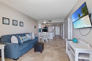 A living room with a blue sofa, a coffee table, and a flat-screen TV mounted on the wall.