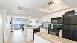 A modern kitchen with white cabinets, granite countertops, a black refrigerator, and a large window overlooking a balcony. - Beachfront 2 Bed at Popular Seawinds! (Marco Island)
