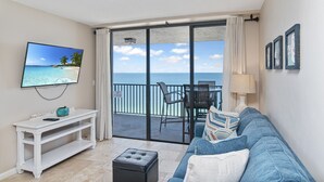 A balcony with a view of the ocean, a white console table, a black ottoman, and a blue sofa with decorative pillows. - Beachfront 2 Bed at Popular Seawinds! (Marco Island)