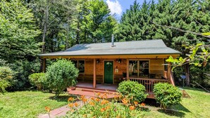 A wooden cabin with a green door, a porch, and a small garden with orange flowers.