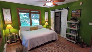 A bedroom with a bed, two bedside lamps, a ceiling fan, a bookshelf, and a window with blinds.