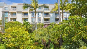 Ein Hotel mit mehreren Balkonen, üppiger tropischer Vegetation und blauem Himmel.