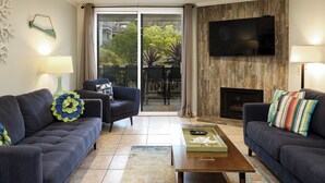 Ein Wohnzimmer mit zwei Sofas, einem Couchtisch, einem an einer Holzwand montierten Fernseher und einem Kamin.