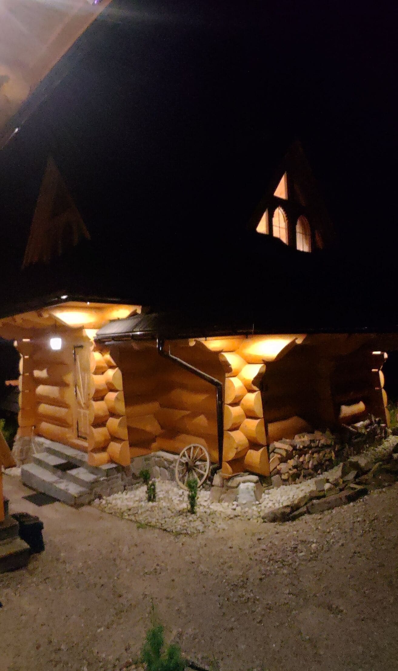 A log cabin with a porch, a wheelbarrow, and a small garden.