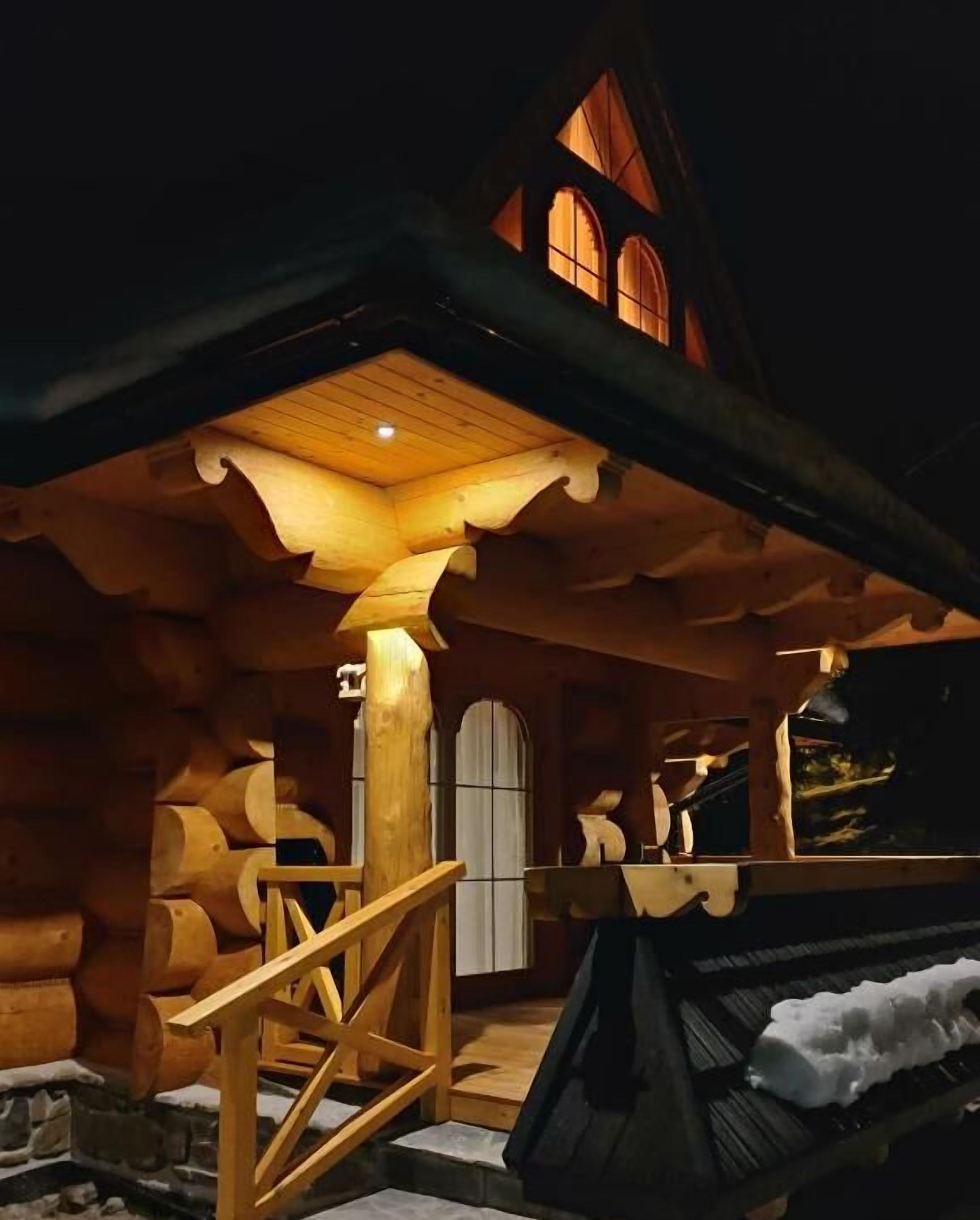 Une cabane en rondins avec un escalier en bois menant à une porte, une cheminée et un mur en pierre.